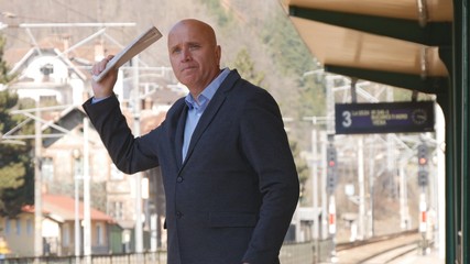 Businessman Gesticulate With a Newspaper in Hand Waiting Train in Railway Statio