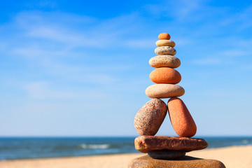 Rock zen pyramid of white and pink pebbles on a background of blue sky and sea.