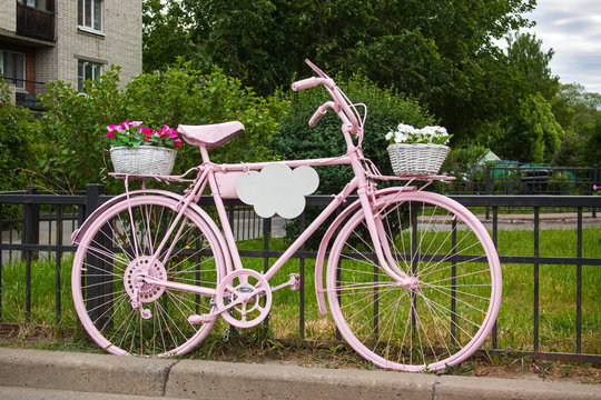 Pink bicycle with flowers baskets long standing next to the fence