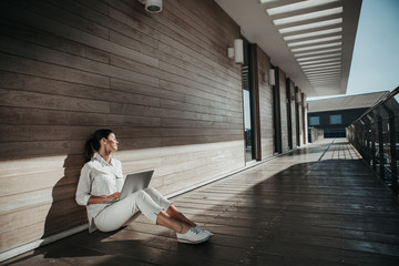 Pleased woman spending good time in open air. She sitting on balcony floor with notebook. Copy space in right side