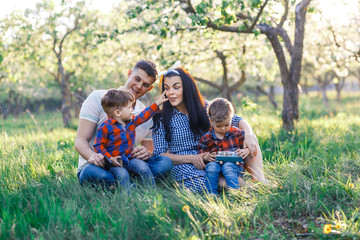Fototapeta premium Happy young family spending time together outside in green nature. Parents playing with twins outside. Family of four walkng in the apple tree garden at the sunset hugging and having fun