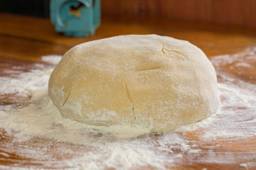 Preparation sweet dough for cookies, pies, cakes. Wad of dough in flour on a wooden table in the kitchen closeup.
