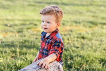 A cute boy with curly hair having fun outside in the country in summer at the sunset. a boy playing in the garden with apple trees and green grass.