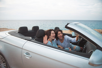 Selfie time. Young delighted women are sitting in cabriolet with open roof and taking picture while...