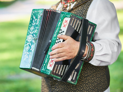 Russian folk instrument - accordion, harmonica in hands of musician, in Slavic national costume with embroidery.
