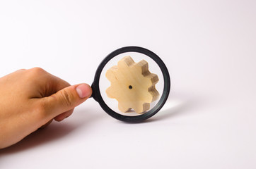 Hand with the magnifying glass is aimed at the wooden wheel gear. concept of studying the technological process and industry, the production chain, the manufactory. Search for parts and spare parts.