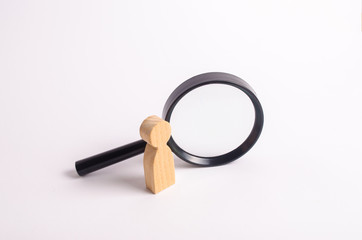 A wooden human figure stands near a magnifying glass on a white background. The concept of the search for people and workers. Search for vacancies and work. Human resources, management.