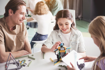 Fototapeta premium Cheerful kids and outgoing man creating robot from constructor during lesson