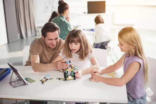 Positive children and outgoing man creating contemporary robot while sitting at table during lesson. Education of future concept
