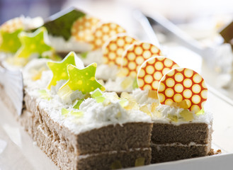 Biscuit cake, decorated with cream, slices of jelly and white chocolate on a white plate. Selective focus