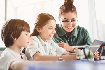 Positive kids and outgoing woman watching at digital device while locating outdoor