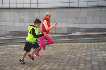 Athletic young woman and boy are running on background of urban landscape. Healthy lifestyle. Family sport.