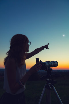 Young woman holding astronomical telescope and looking at the sky.