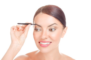 woman with short hair plucking eyebrows with tweezers