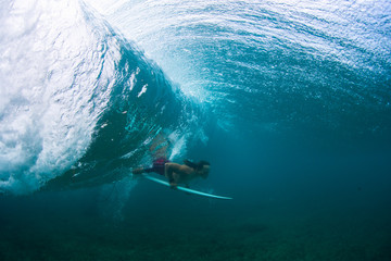 Underwater view of the young male surfer passing the ocean wave with surf board