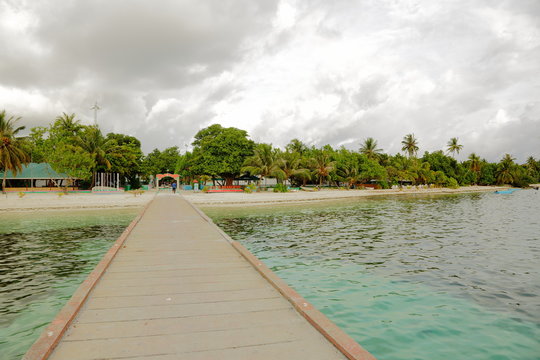 Beautiful view of island coast with wooden pier over turquoise water. Green trees and white clouds on background. Maldives, Dhangethi Island, Indian Ocean.