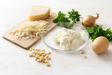 ingredients for a ricotta parmesan souffle with pine nuts, onion and parsley on a white wooden table