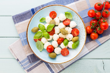 Delicious caprese salad with ripe cherry tomatoes and mini mozzarella cheese balls with fresh basil leaves.