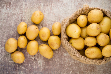 Sack of fresh raw potatoes on wooden background, top view