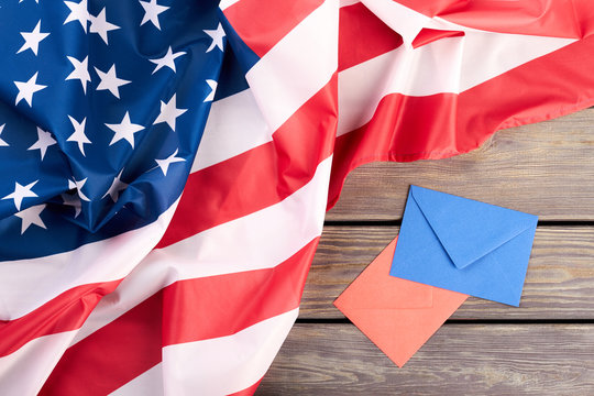 USA flag, red and blue envelopes. Crumpled American flag and colorful envelopes on wooden background.