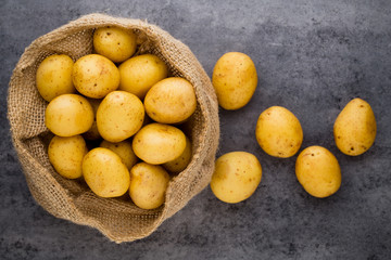 Sack of fresh raw potatoes on wooden background, top view