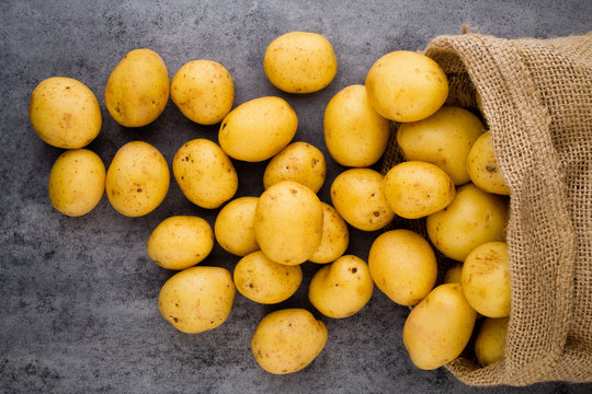 Sack of fresh raw potatoes on wooden background, top view