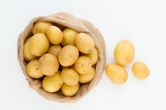 Sack of fresh raw potatoes on wooden background, top view