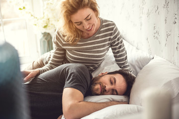 Blessed woman is looking at her partner while he is sleeping. She is gently touching him and he is calmly lying in comfortable bed asleep. Caring woman concept