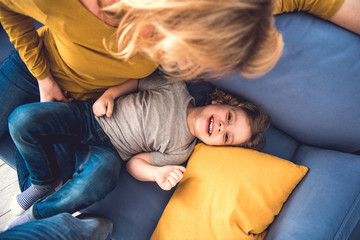 Top view of laughing son spending great time and looking at camera with joy. He is lying on sofa...