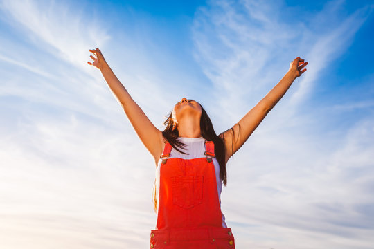 Happy and free young woman raising arms on blue sky background. Freedom. Healthy lifestyle