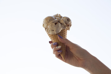 Woman's hand held caramel ice cream to summer sky, horizontal