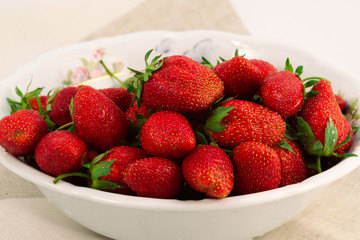 Ripe red strawberry with green leaves in a round porcelain plate.
