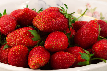 A large ripe strawberry with green leaves, stacked with a slide in a plate.