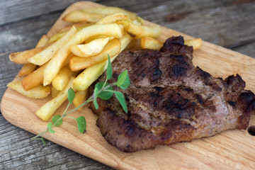 Grilled pork steak with french fries and oregano over wooden background