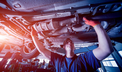 Car mechanic examining car suspension of lifted automobile at repair service station