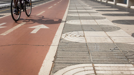 Cyclist shadow on bicycle red lane next to pedestrian sidewalk on the coast in Las Palmas, Spain....