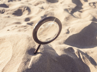 buried magnifying glass in sand on a summer day