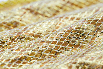 Holiday background image of gold sparkly mesh ribbon on metallic fabric with copy space. Macro with extremely shallow dof.