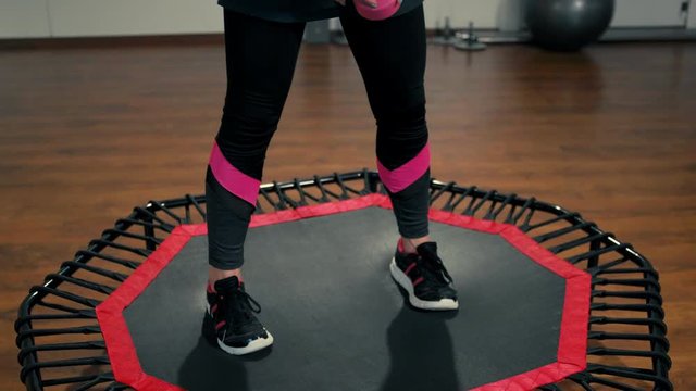 Young Beautiful Lady is Doing Sport Exercise with Dumbbells on Mini Trampoline in the Gym