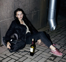 young poor ttenage girl sitting at dirty wall on floor with bott