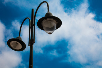 Light post with two bulbs and blue cloudy sky background. Outdoor street lights. Cast iron lamp. Large lantern. Lighting pole. Illuminate. Electrical device