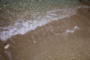Wavy foamy crystal clear ocean water washing up on sandy beach shore. White waves on sand. Relaxation. Summer vacations. Leisure. Traveling abroad in Corfu Greece