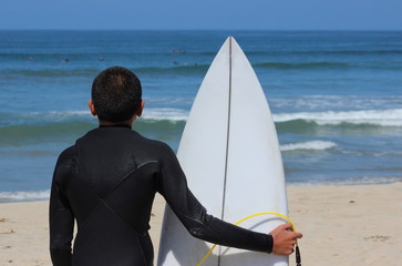 A young boy surfer holds his board and looks at waves