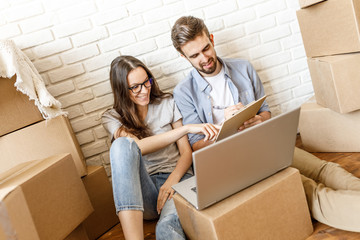 Laughing girl and man taking notes on clipboard while moving to new place and sitting with boxes...