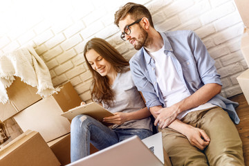 Young girl doing checklist while sitting with man among boxes and laptop ready for moving. 
