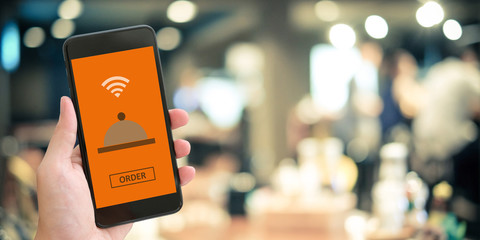 Hand holding smart phone with food online on screen over blur restaurant background with copy space, mock up, template, food online concept