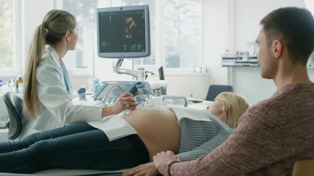 In the Hospital, Obstetrician Uses Transducer for Ultrasound/ Sonogram Screening Belly of the Pregnant Mother. Husband Supports His Wife and Holds Her Hand. Shot on RED EPIC-W 8K Helium Cinema Camera.
