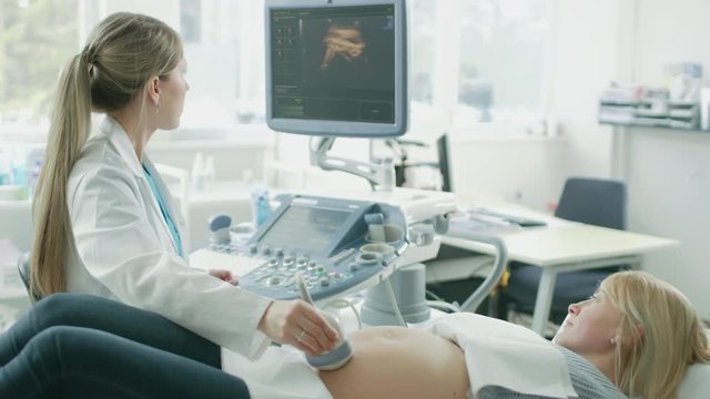In the Hospital, Pregnant Woman Getting Ultrasound / Sonogram Scan, Obstetrician Explains Procedure to Her and Her Supportive Husband. Happy Family Waiting for their First Baby. 