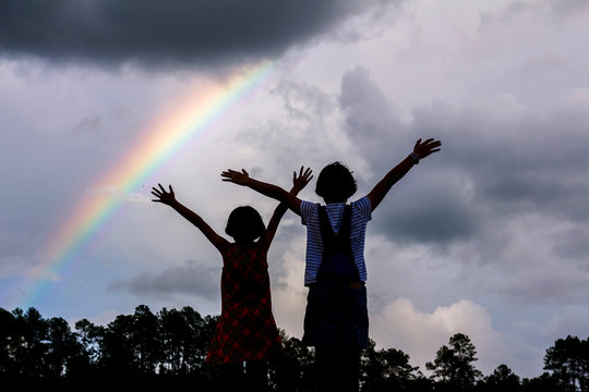 Children Playing Under Cloudy Sky With Rainbow.