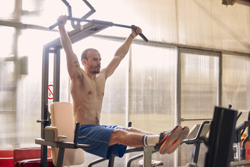 one young man, stationary machine, pull-up exercise, legs extended, abs core exercise.